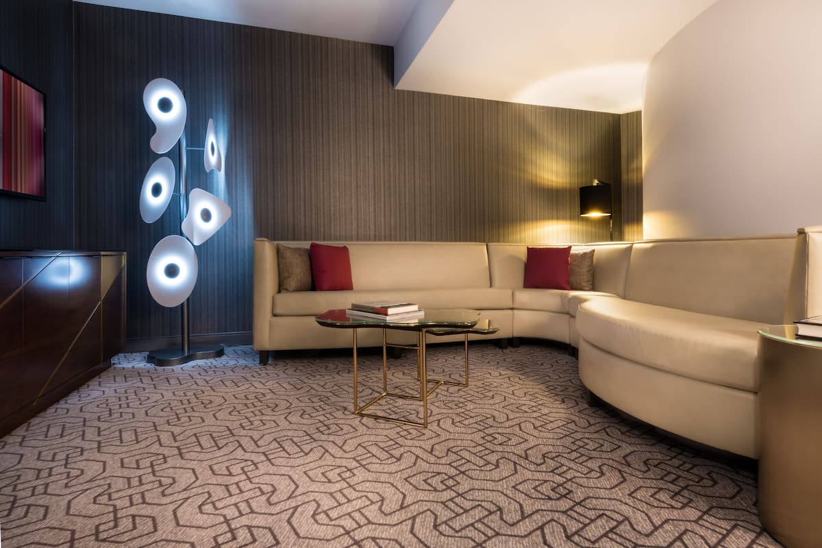 A modern living room with a curved sofa, a glass coffee table, and a patterned carpet.