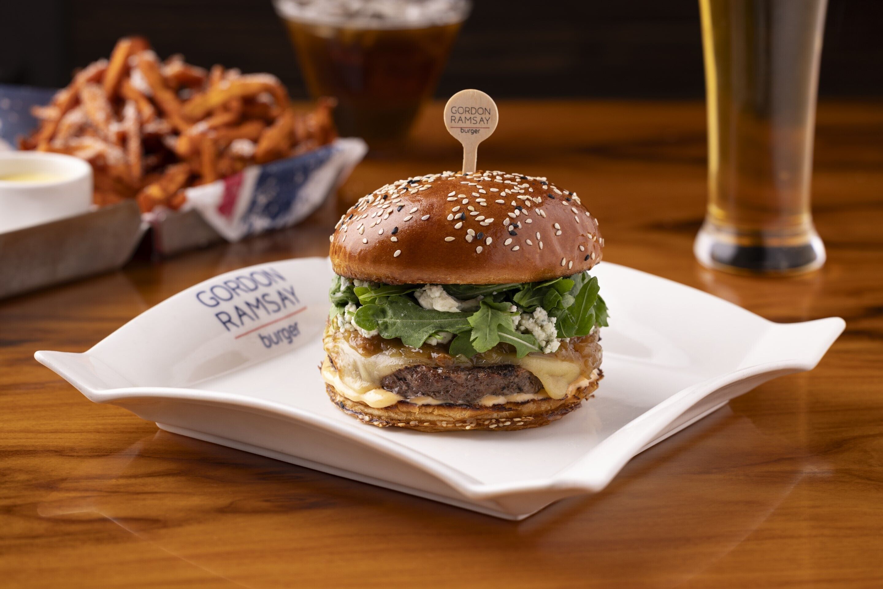 En hamburgare på en vit tallrik med en etikett där det står ”Gordon Ramsay Burger”.