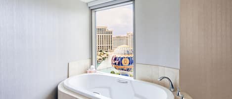 A bathroom with a large bathtub, a window with a view of a cityscape, and a decorative globe.