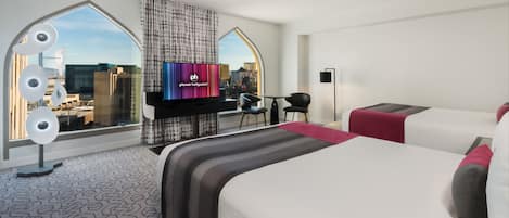 Habitación de hotel con una cama grande, televisor, escritorio y vista a la ciudad.