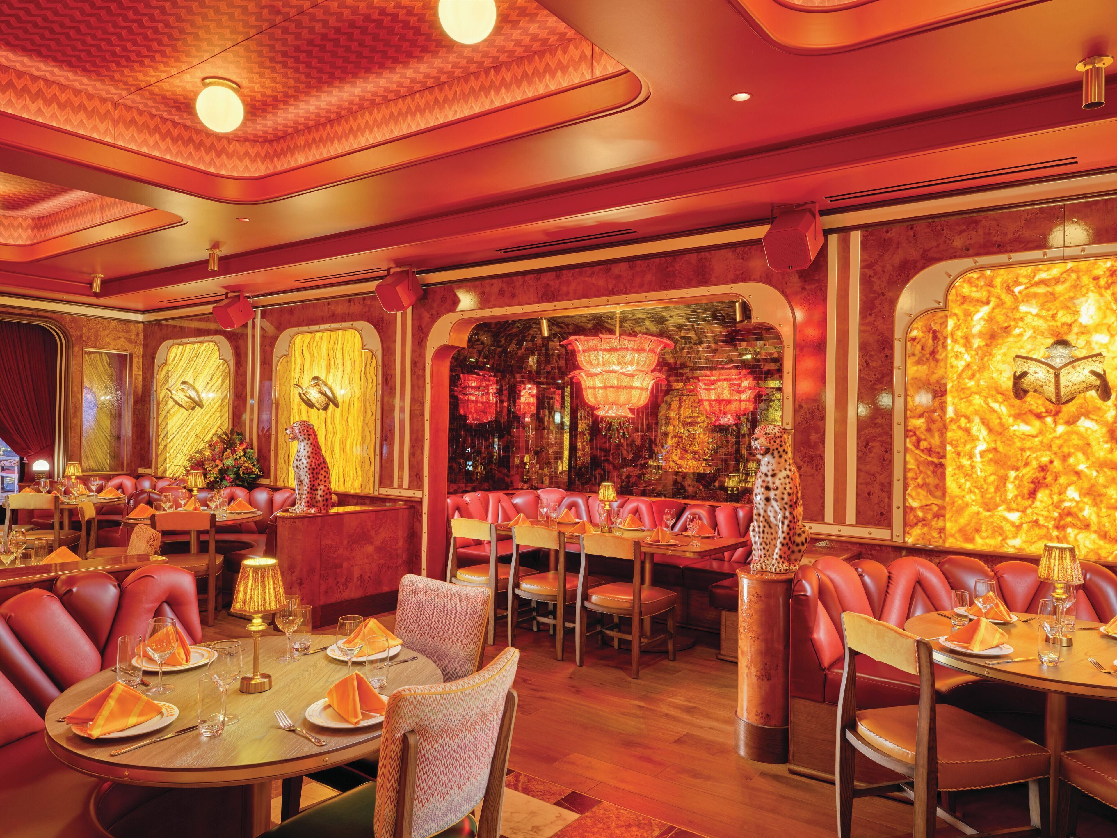 A restaurant with red leather booths, round tables, and a warm, red-hued interior.