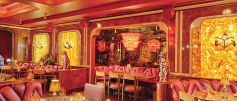 A restaurant with red leather booths, round tables, and a warm, red-hued interior.