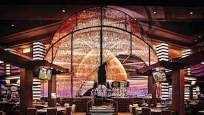 A casino interior with a large, illuminated wall structure, multiple gaming tables, and a bar area. - Planet Hollywood Resort & Casino (Las Vegas)