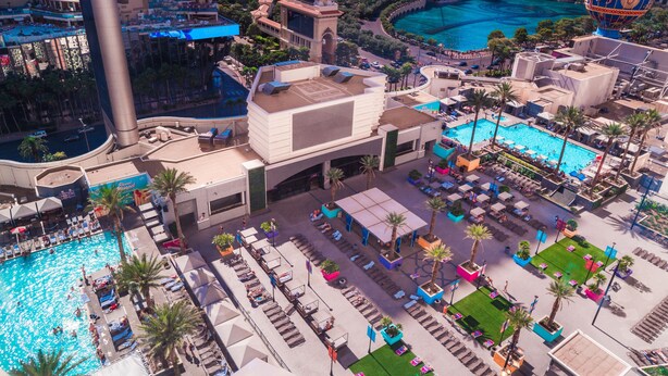 An aerial view of a hotel with a large pool area, multiple lounge chairs, and a prominent bell tower. - Planet Hollywood Resort & Casino (Las Vegas)