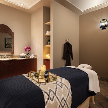 A hotel room with a large bed, a vanity with a mirror, a nightstand, and two wall sconces.