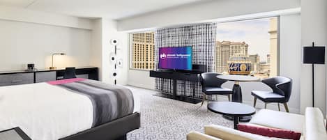 A hotel room with a bed, a desk, a TV, and a view of the city.