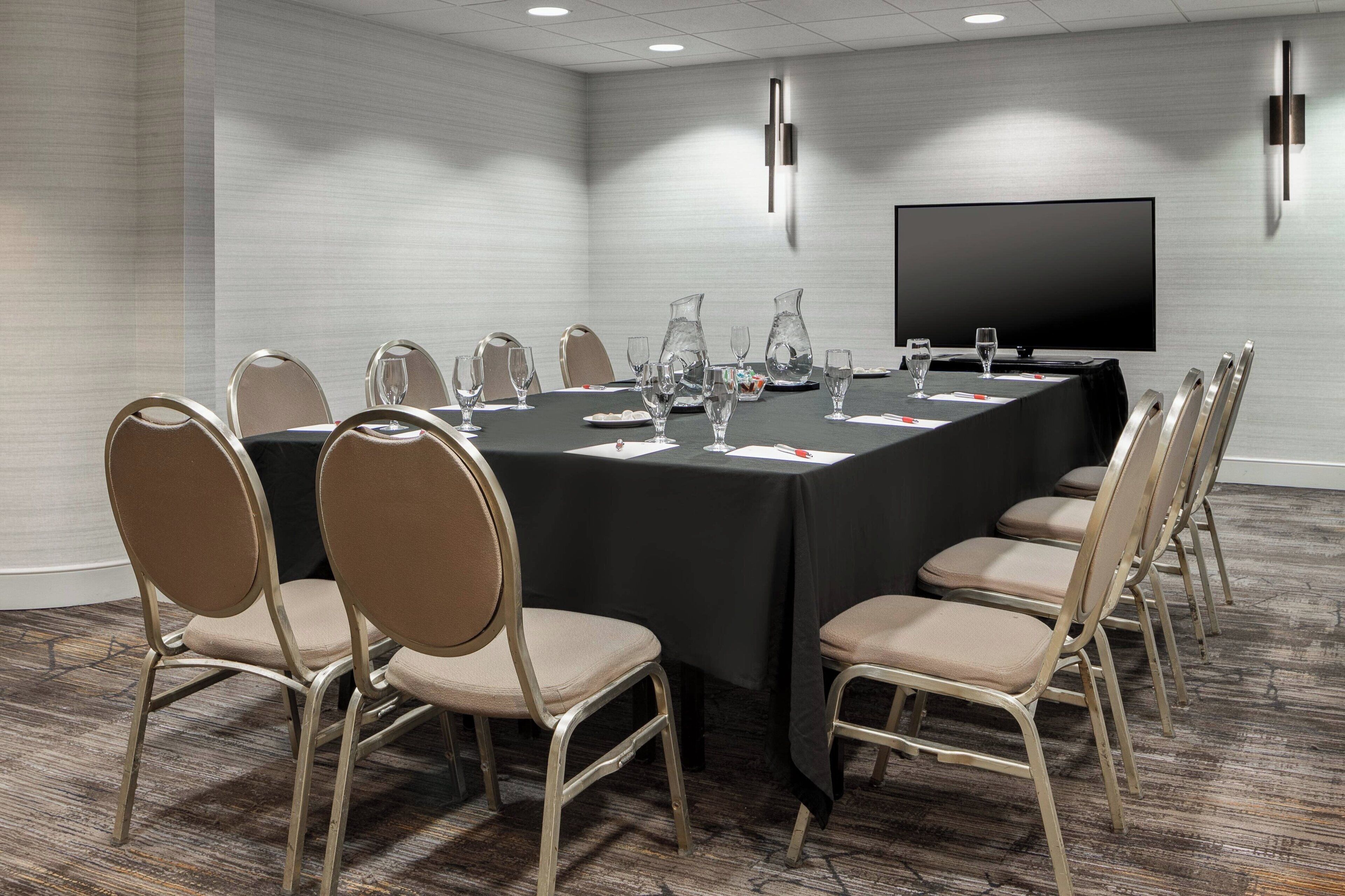 A conference room with a long table, chairs, a flat-screen TV, and a projector.
