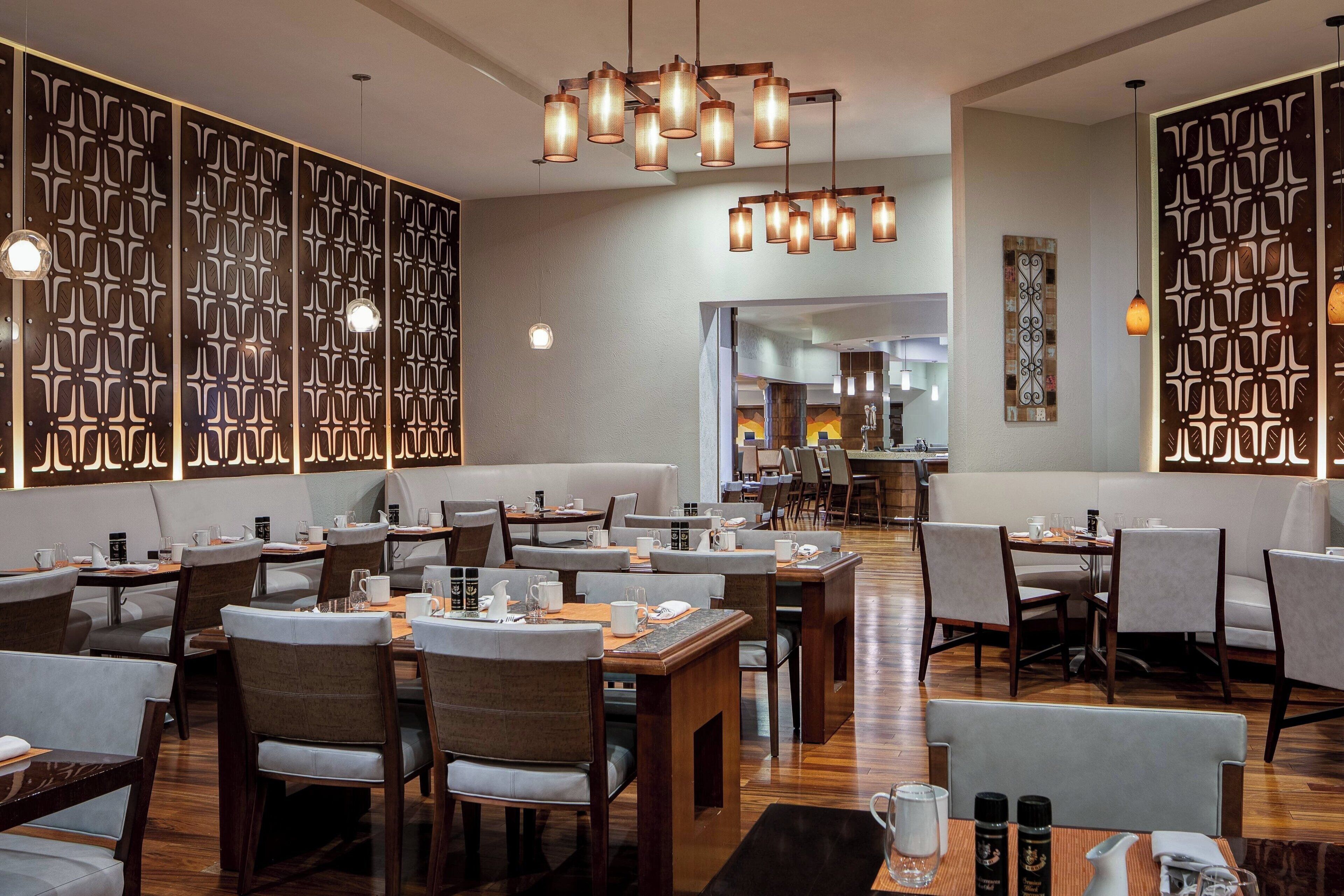 A modern restaurant with wooden tables and chairs, decorative wall panels, and hanging pendant lights.