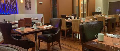 A restaurant with wooden tables and chairs, a blue decorative wall, and a modern chandelier.