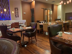 A restaurant with wooden tables and chairs, a blue decorative wall, and a modern chandelier.