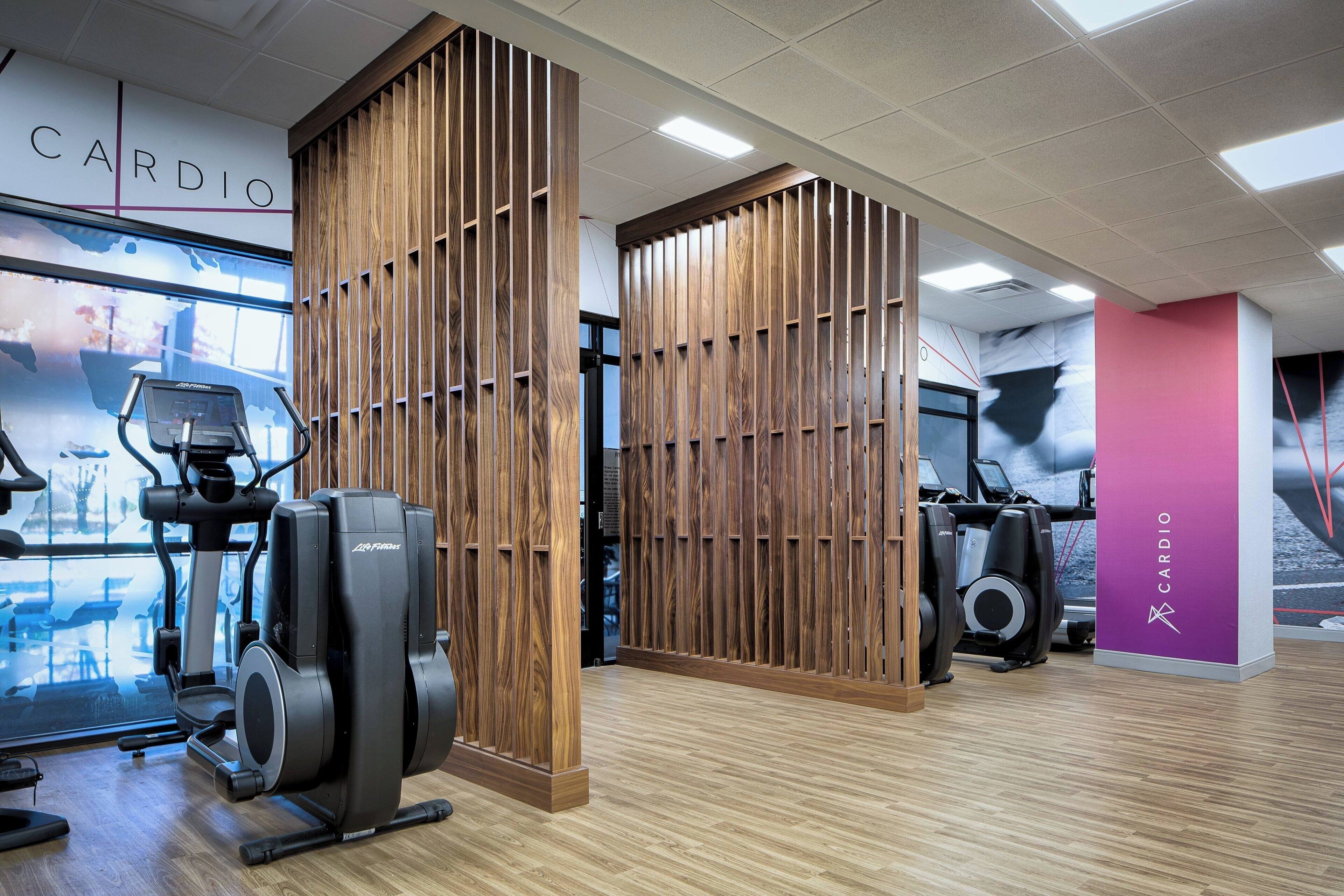 Un gimnasio con equipamiento cardiovascular, paneles de madera y un letrero que dice 'CARDIO'.