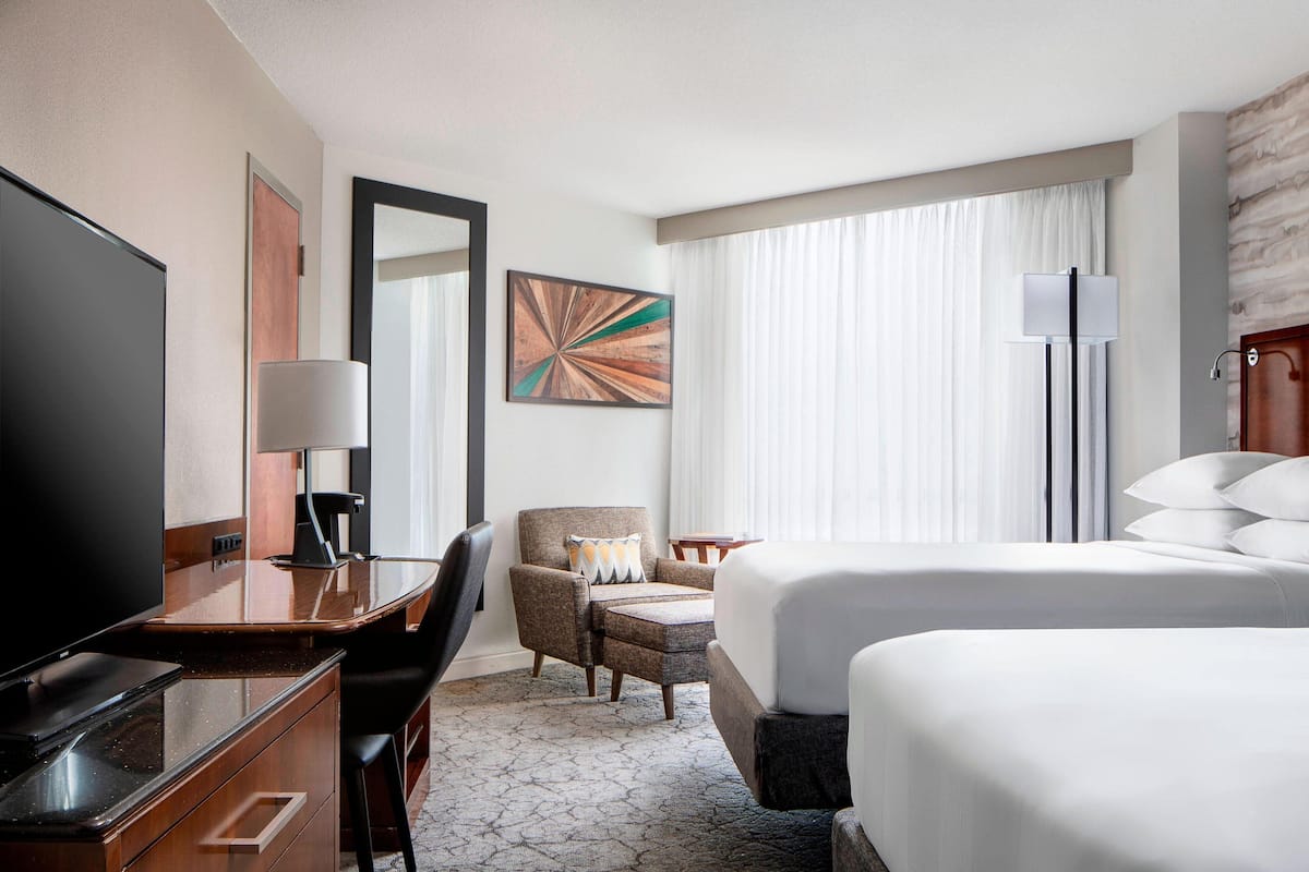 A hotel room with a bed, a desk with a TV, a chair, a lamp, and a painting on the wall.