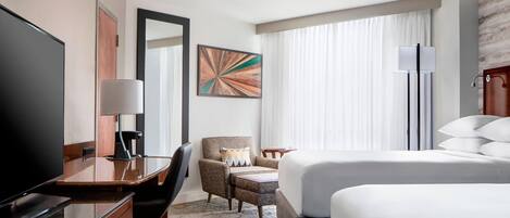 A hotel room with a bed, a desk with a TV, a chair, a lamp, and a painting on the wall.