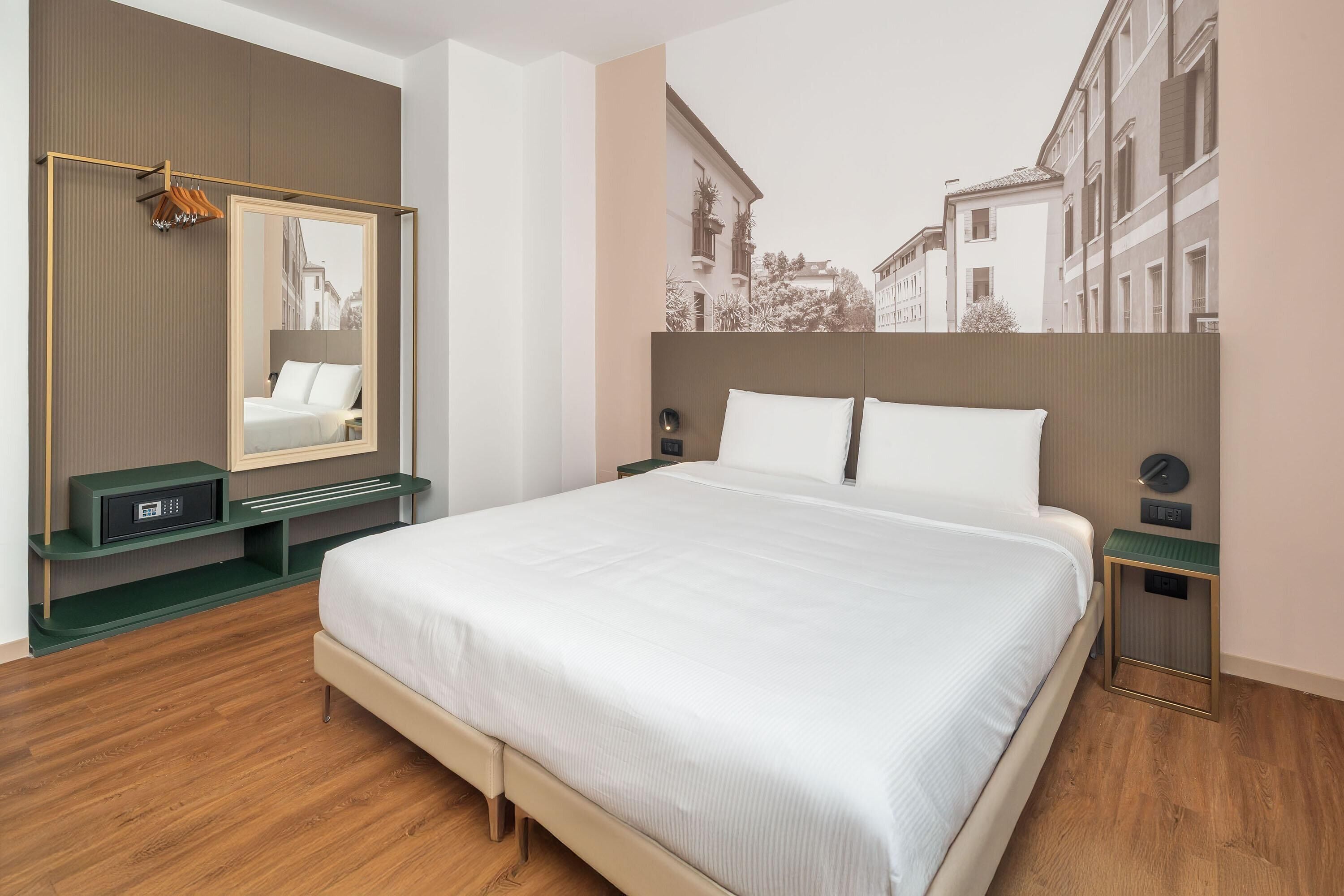 A hotel room with a large bed, a mirror, a nightstand, and a wall-mounted TV.