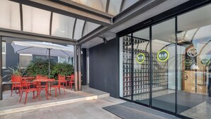 An outdoor seating area with red chairs and a white umbrella, a glass door entrance with B&B Hotels signage, and a modern building facade. - B&B Hotel Treviso Al Fogher (Treviso)