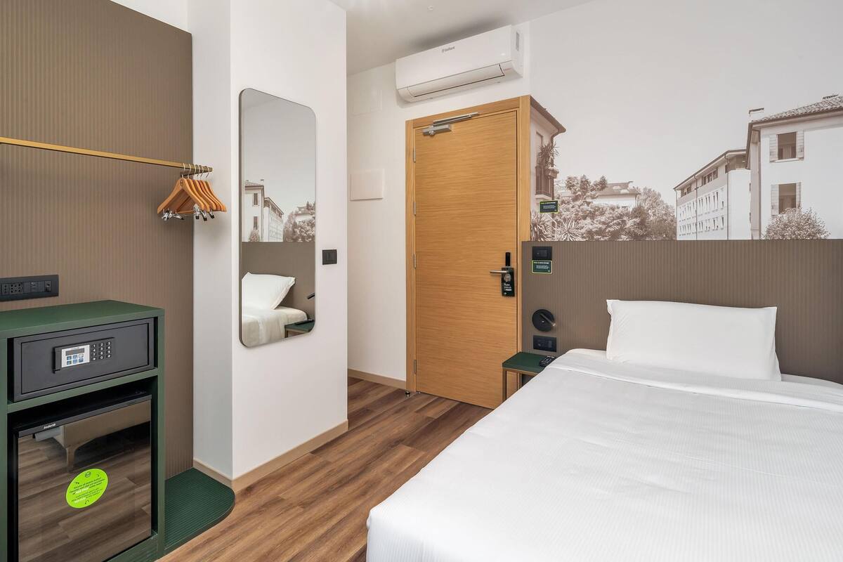 Ein Hotelzimmer mit Bett, Schreibtisch mit Computer, Spiegel, Kleiderschrank und Klimaanlage.