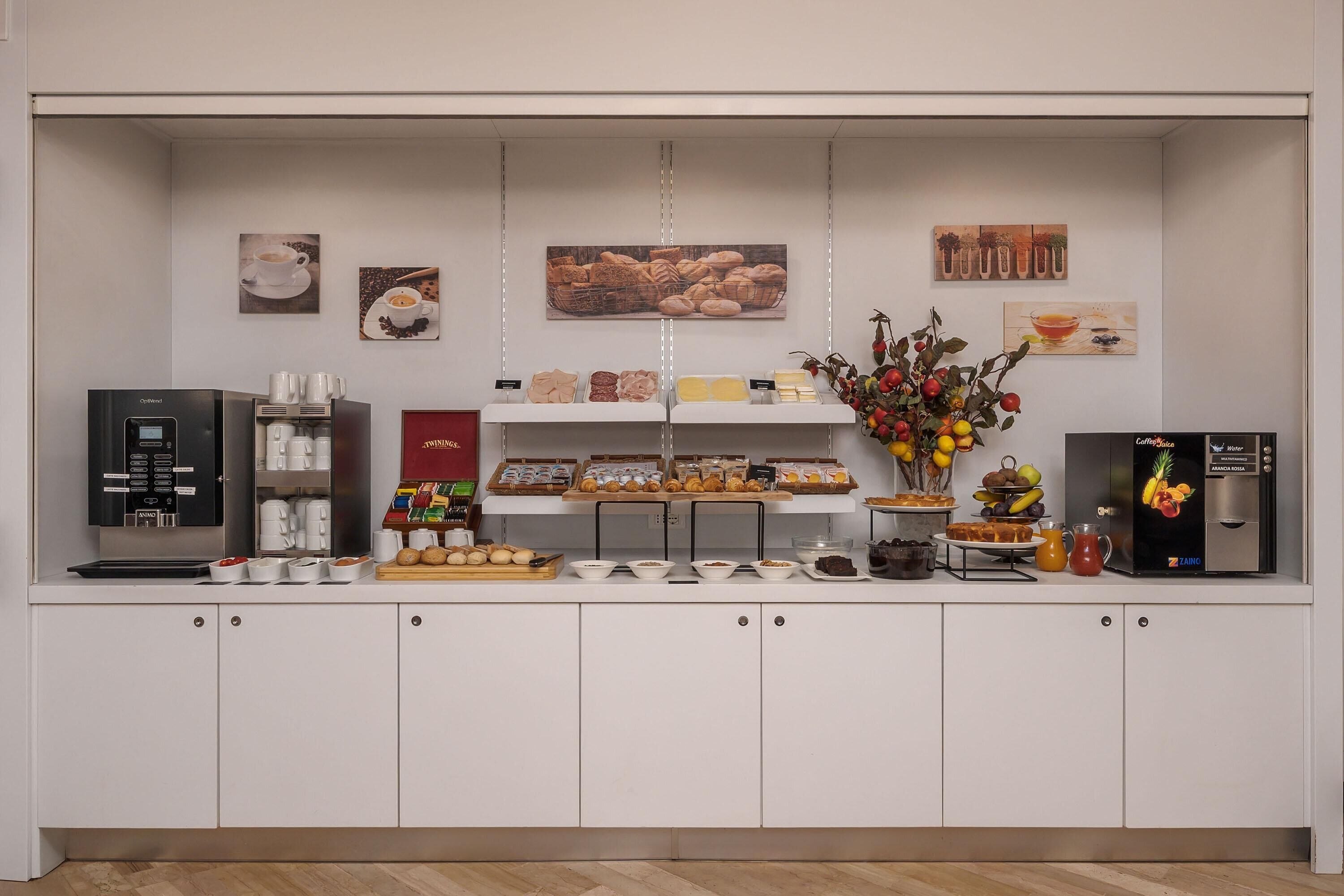 A breakfast bar with a coffee machine, a selection of pastries, and a fruit display.