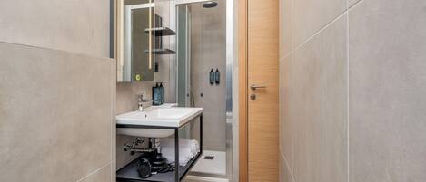 A modern bathroom with a built-in sink, a shower enclosure, and a wooden door.
