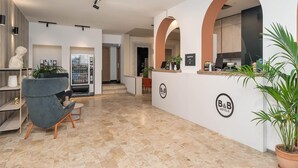 A modern hotel lobby with a reception desk, a marble-tiled floor, and a grey armchair. - B&B Hotel Treviso Al Fogher (Treviso)