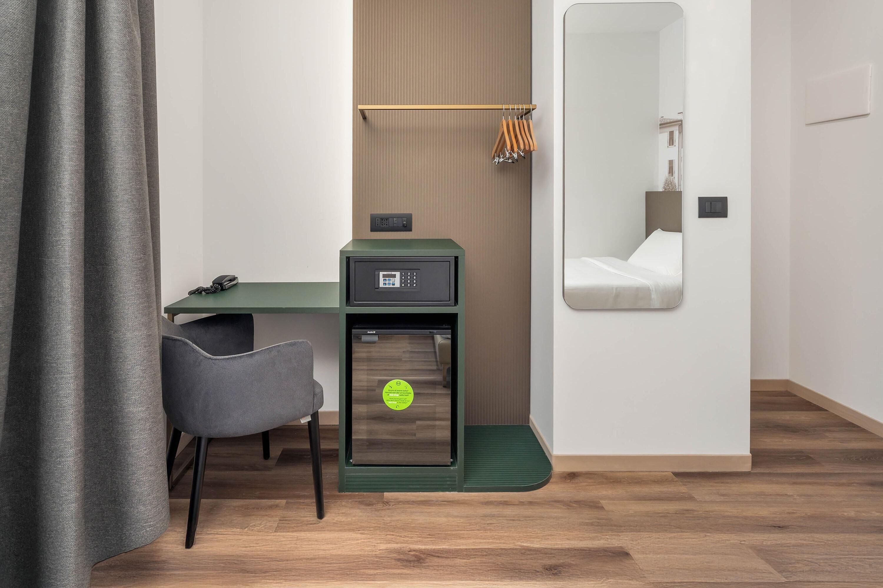Une chambre d’hôtel de taille réduite, équipée d’un bureau, d’une chaise et d’un petit coffre-fort.