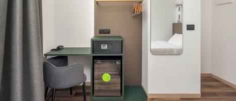 Une chambre d’hôtel de taille réduite, équipée d’un bureau, d’une chaise et d’un petit coffre-fort.