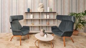 A modern living room with two grey armchairs, a round coffee table, and a striped wallpaper background. - B&B Hotel Treviso Al Fogher (Treviso)
