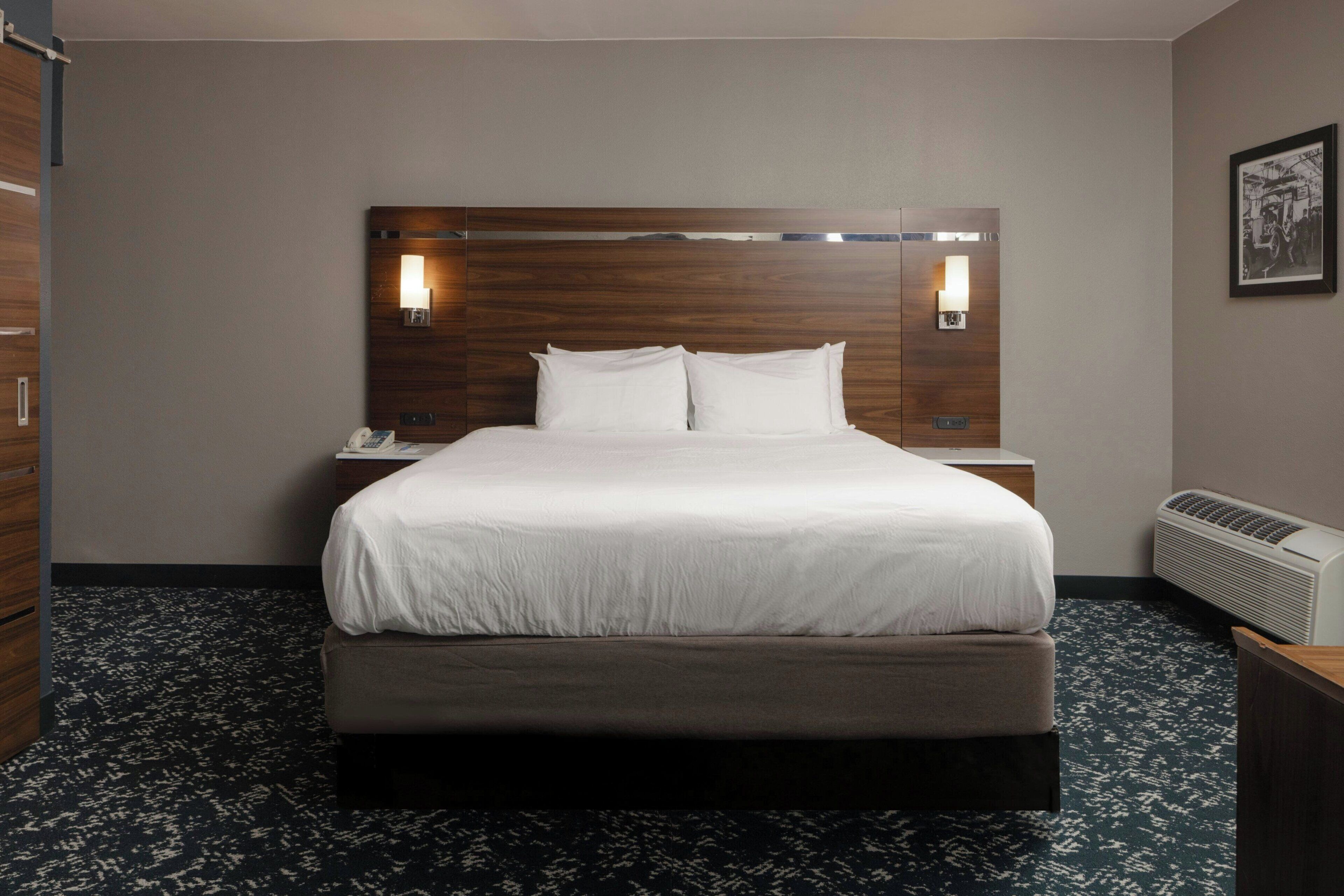 A hotel room with a large bed, bedside lamps, a telephone, and a wall-mounted heater.