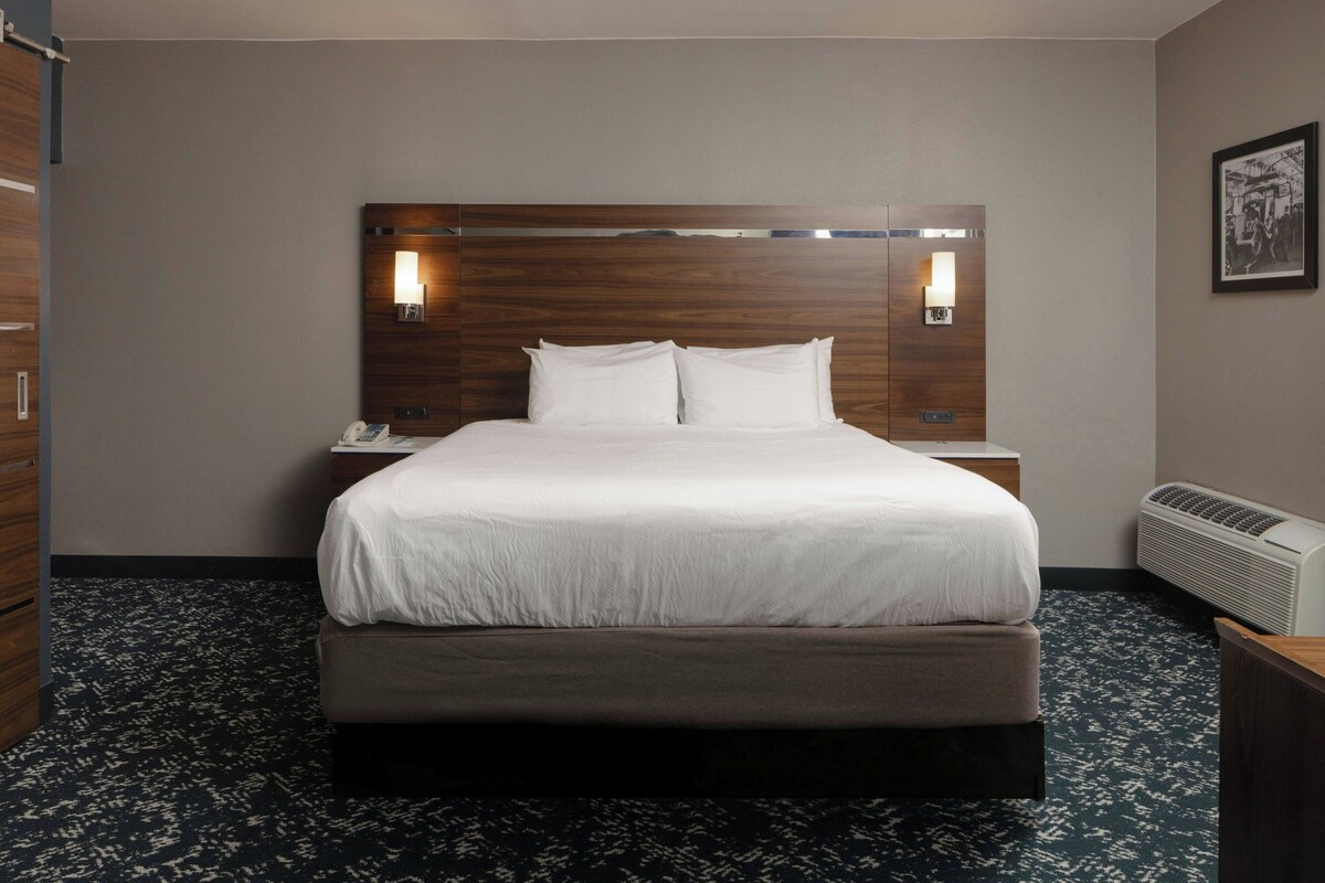 A hotel room with a large bed, bedside lamps, a telephone, and a wall-mounted heater.