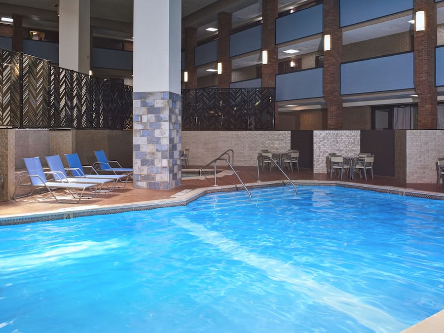 A hotel pool area with a clear blue pool, lounge chairs, and a seating area with tables and chairs.