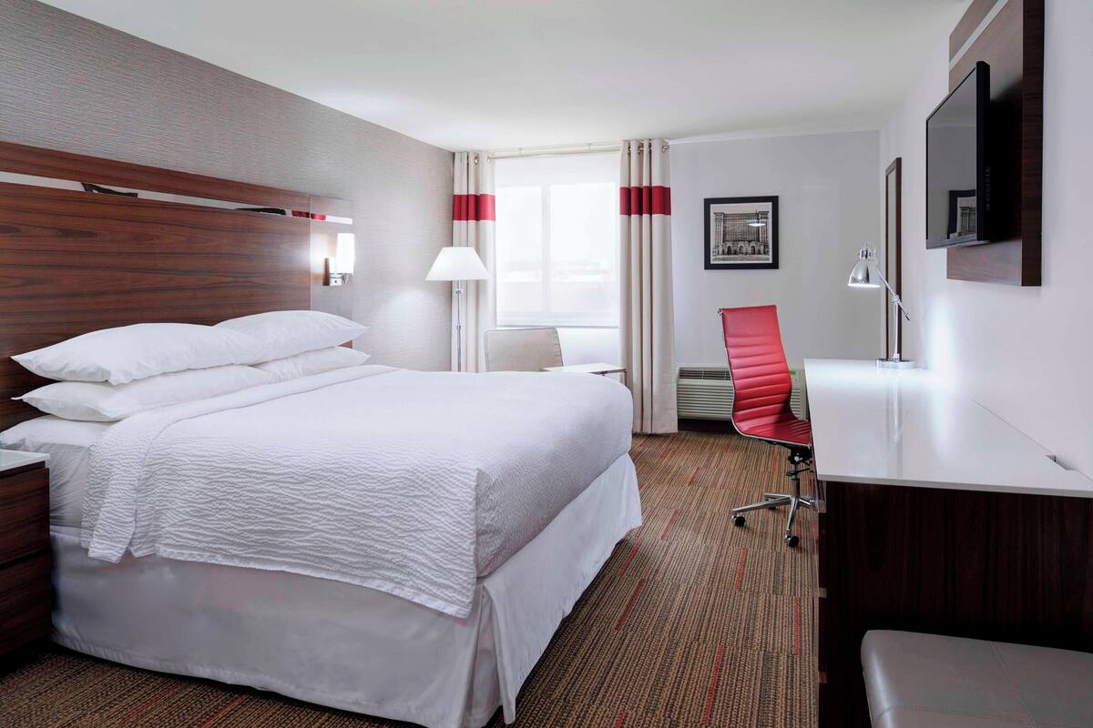 Una habitación de hotel con una cama grande, un escritorio, una silla y un televisor en la pared.