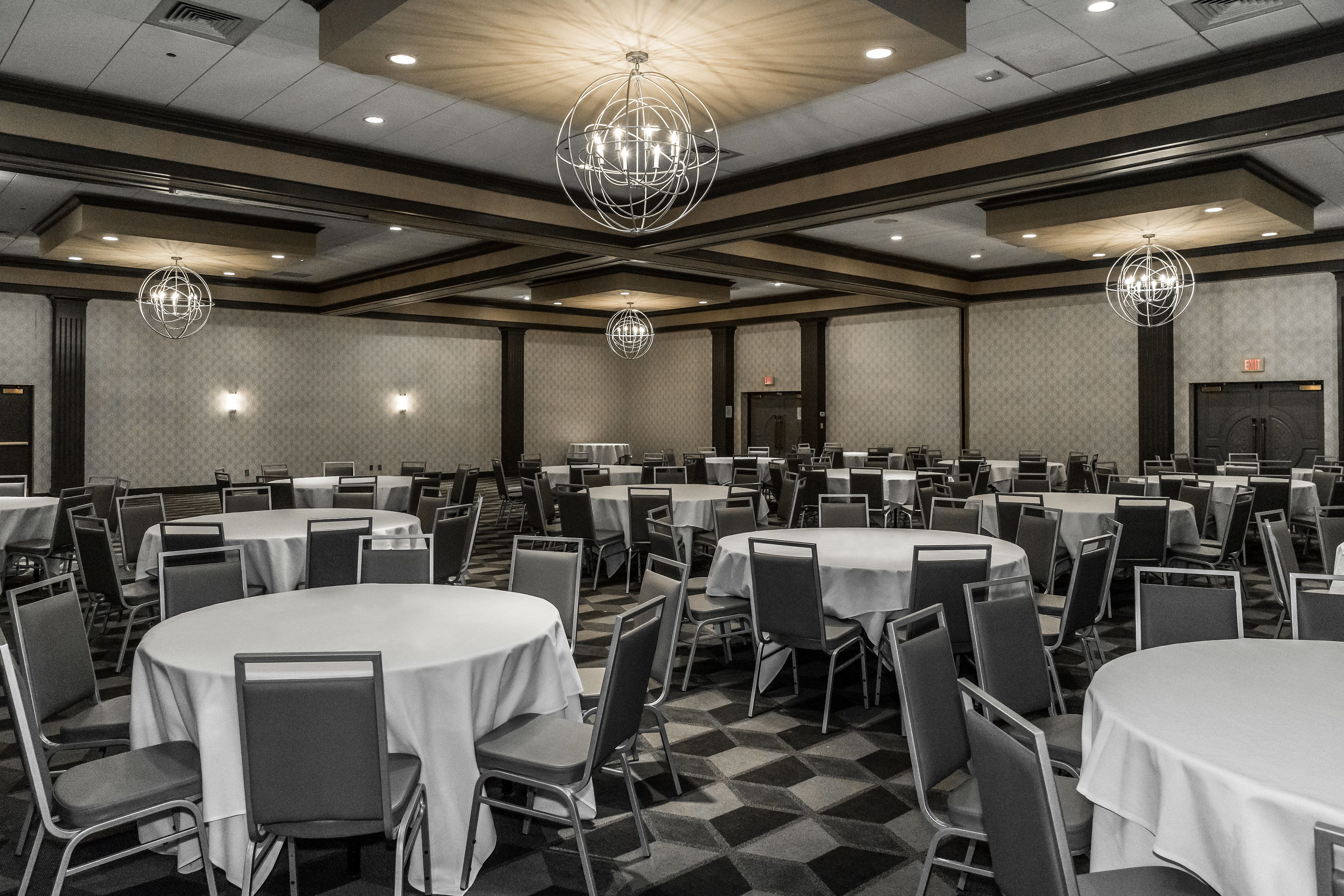 A large banquet hall with round tables and chairs, high ceilings, and modern chandeliers.