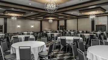 A large banquet hall with round tables and chairs, high ceilings, and modern chandeliers.