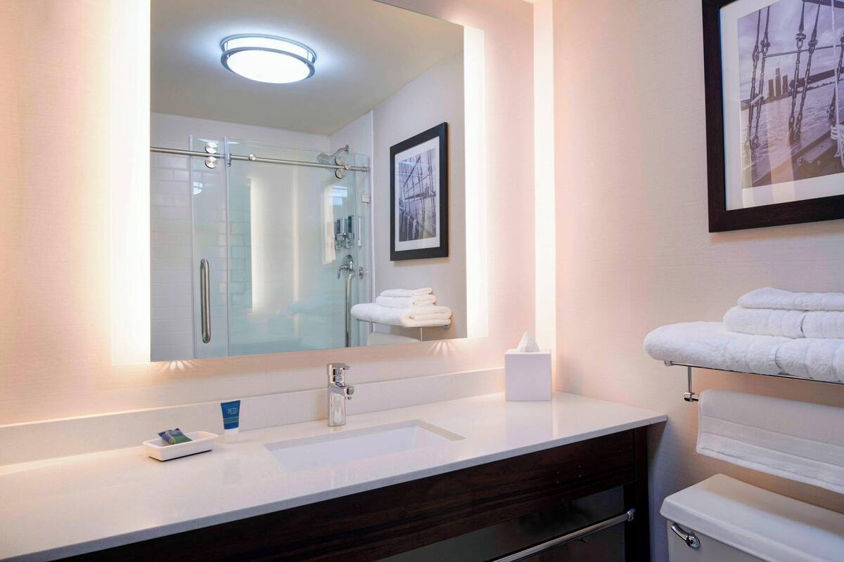 Un baño moderno con un espejo grande, un lavabo blanco, una cabina de ducha de vidrio y un perchero con toallas dobladas cuidadosamente.