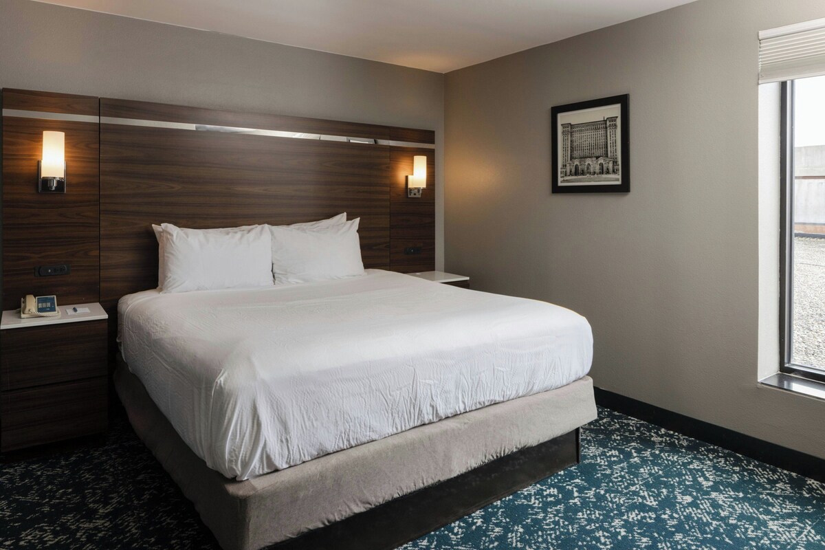 A hotel room with a large bed, two bedside tables, a nightstand, a wall-mounted lamp, and a framed picture on the wall.
