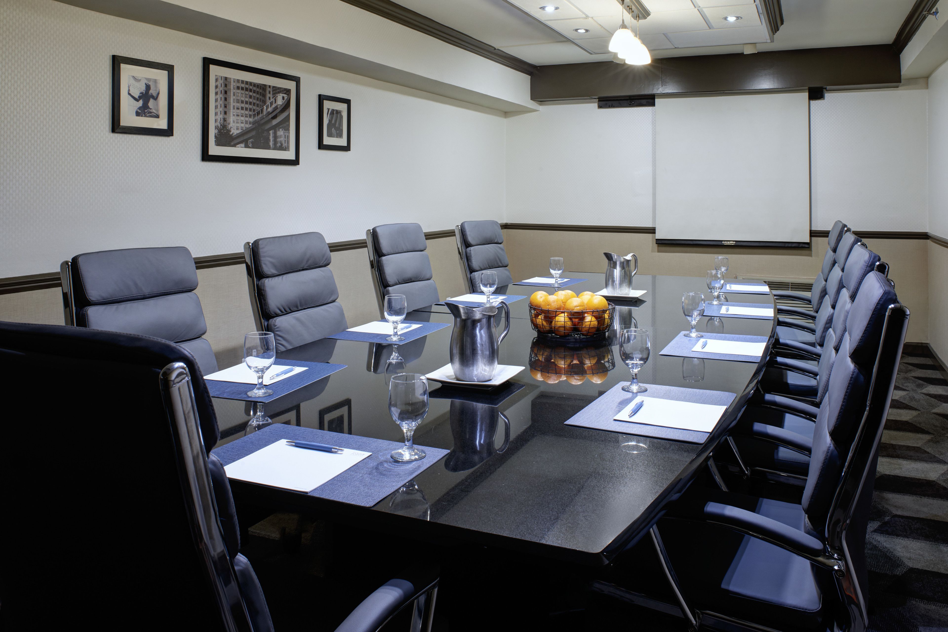Uma sala de conferências com uma mesa grande, várias cadeiras e uma tela de projetor.