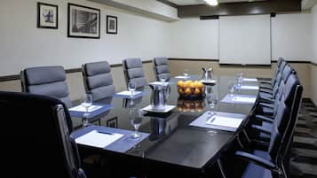 Uma sala de conferências com uma mesa grande, várias cadeiras e uma tela de projetor.