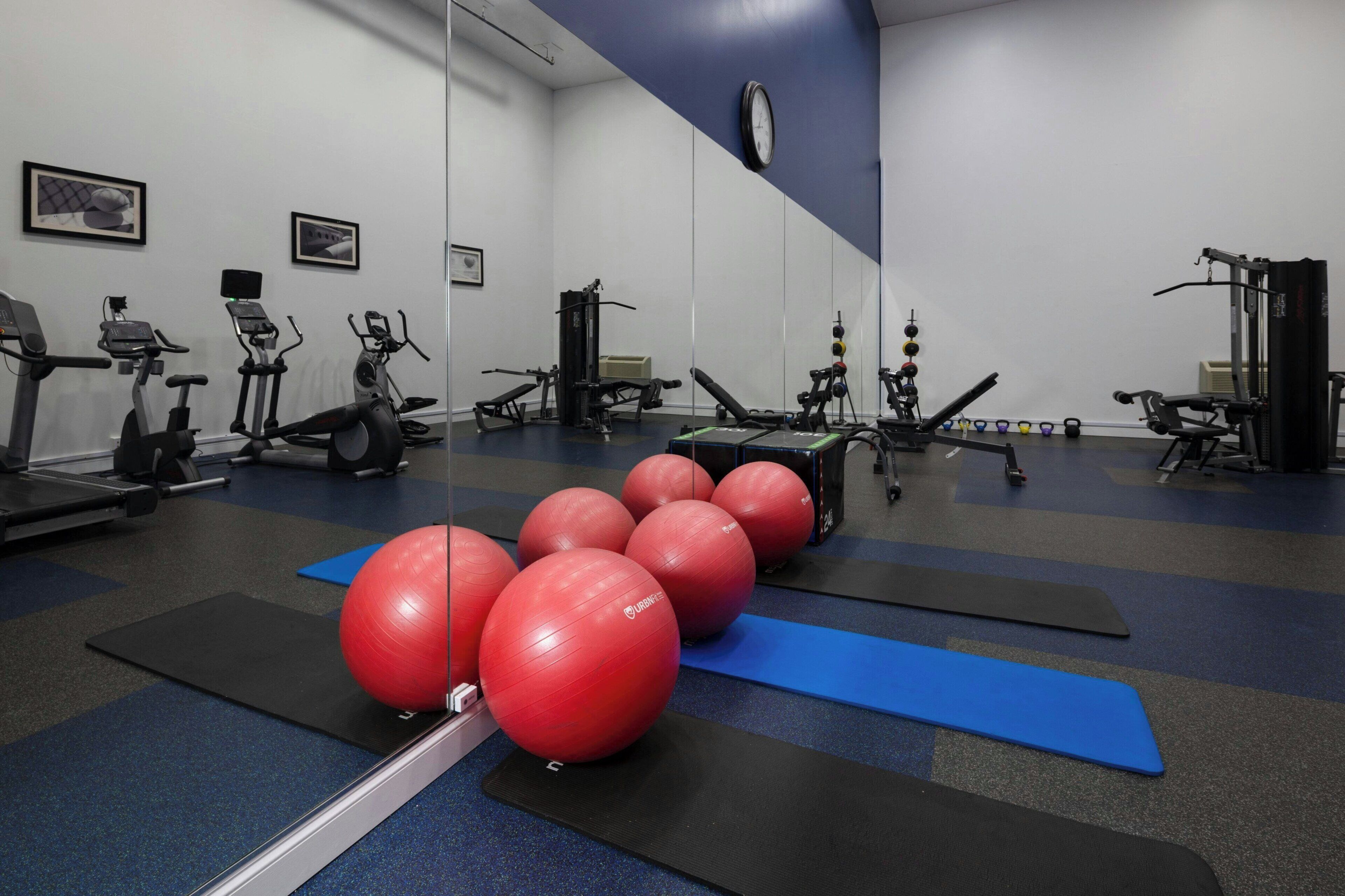 A gym with exercise equipment, red exercise balls, and blue mats.