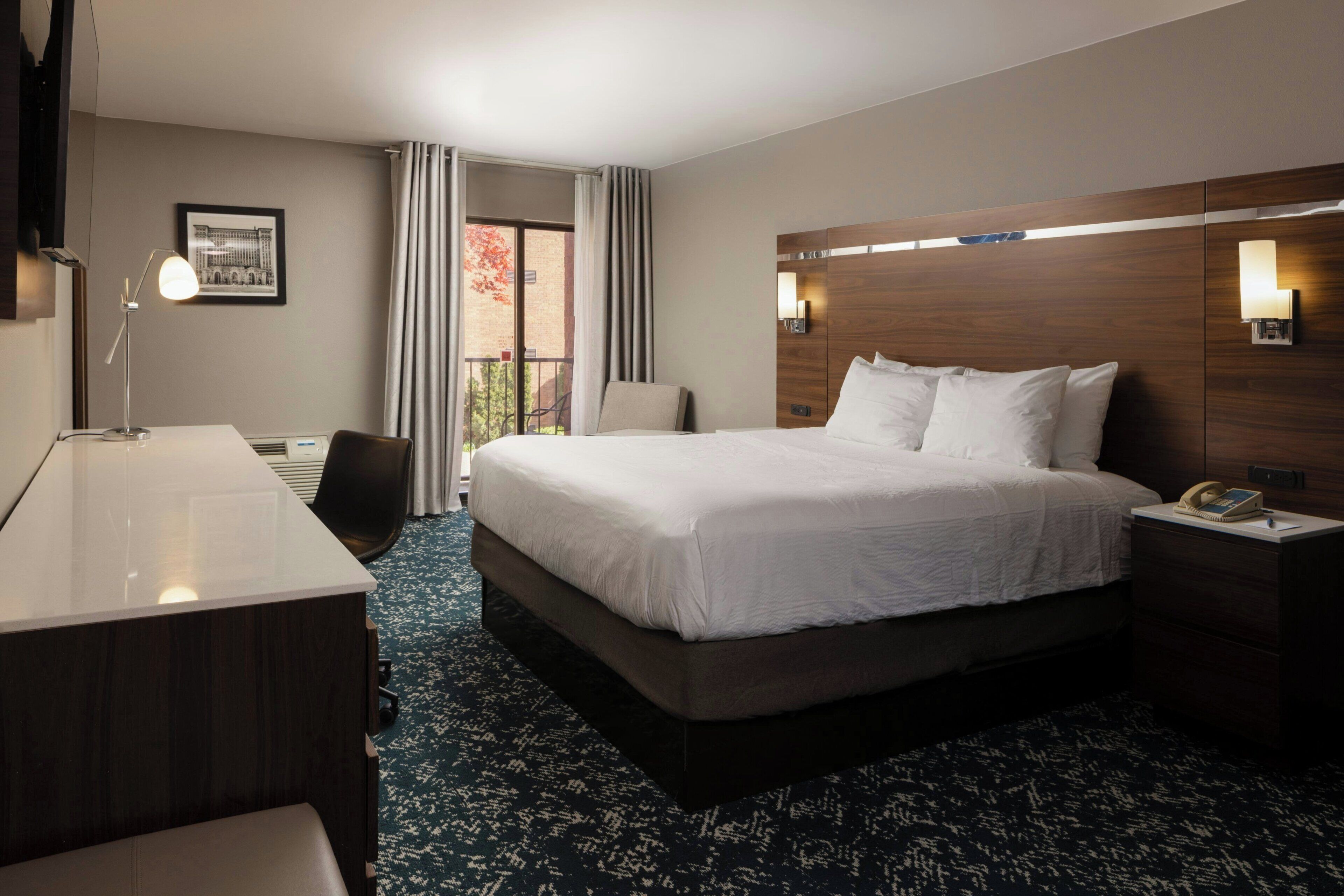 A hotel room with a bed, desk, chair, and a view of the outside.