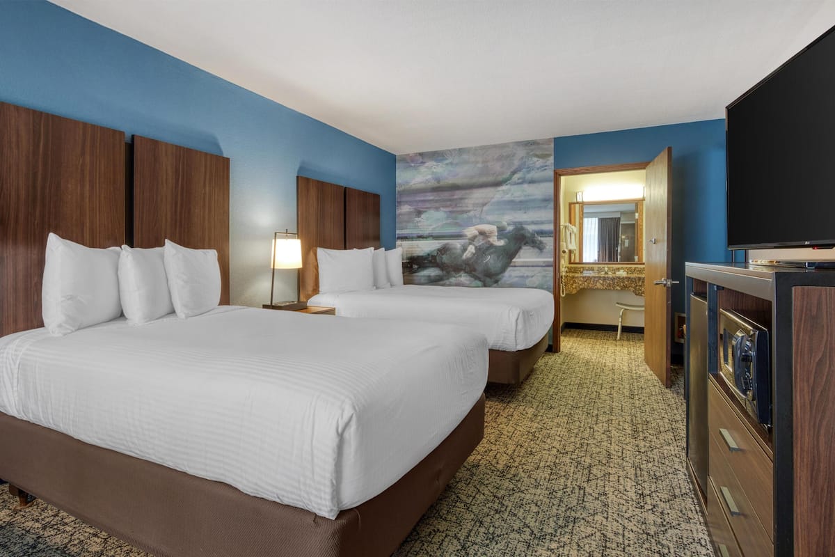 A hotel room with two beds, a television, a mirror, and a painting on the wall.