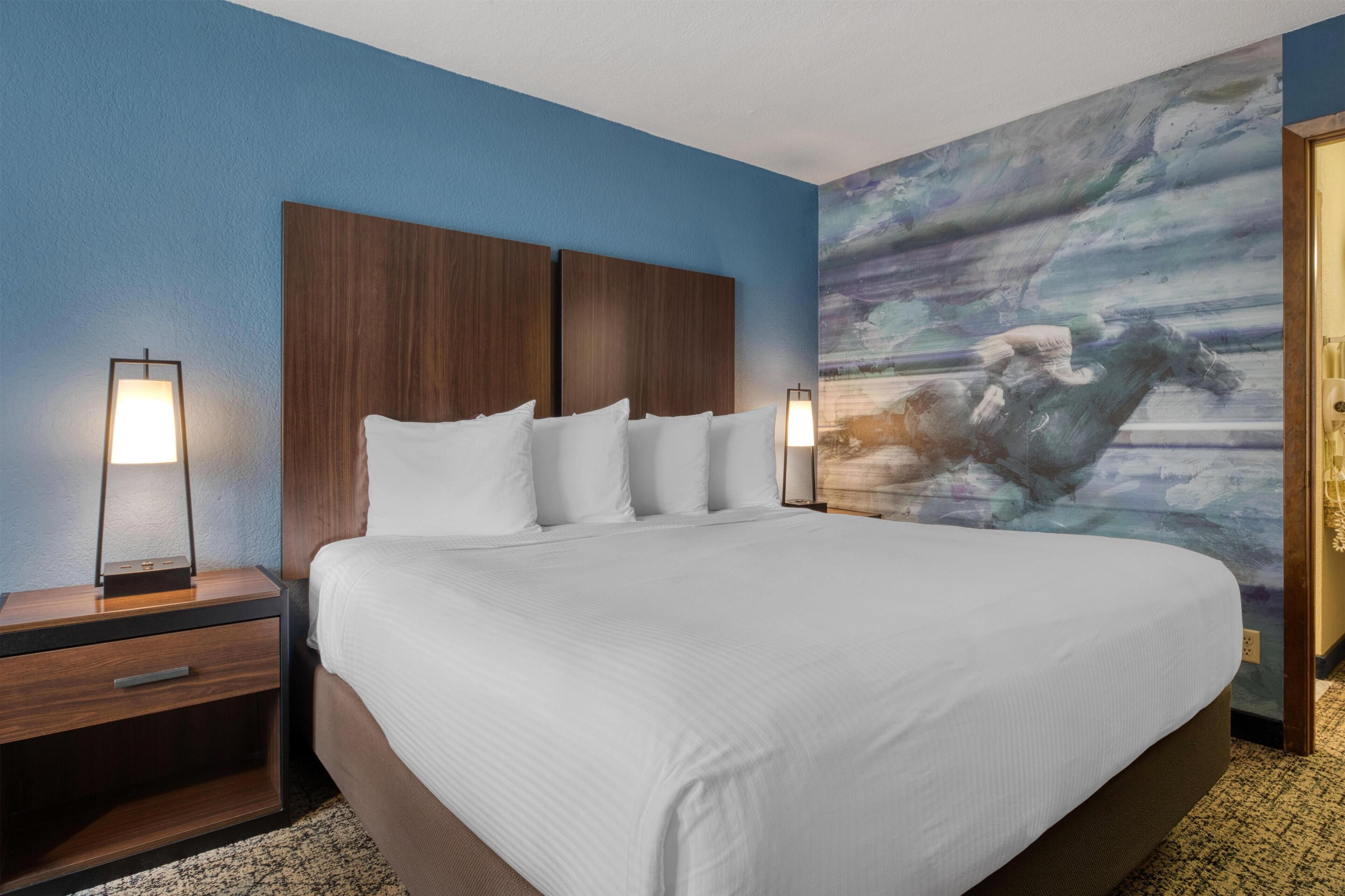 A hotel room with a large bed, two bedside tables with lamps, and a wall mural.