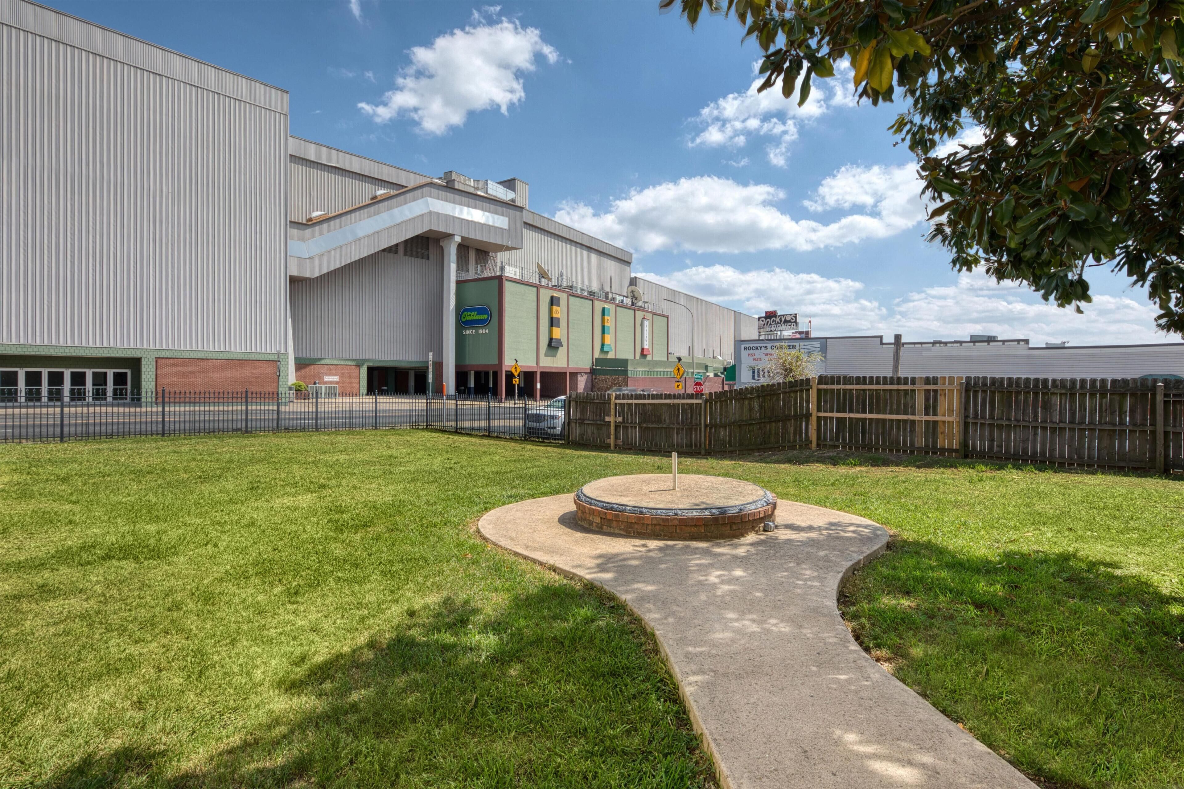 A large industrial-style building with a fenced courtyard, a paved walkway, and a small circular feature in the center.