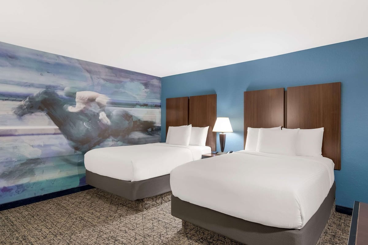 A hotel room with two beds, a large abstract painting on the wall, and a blue accent wall.