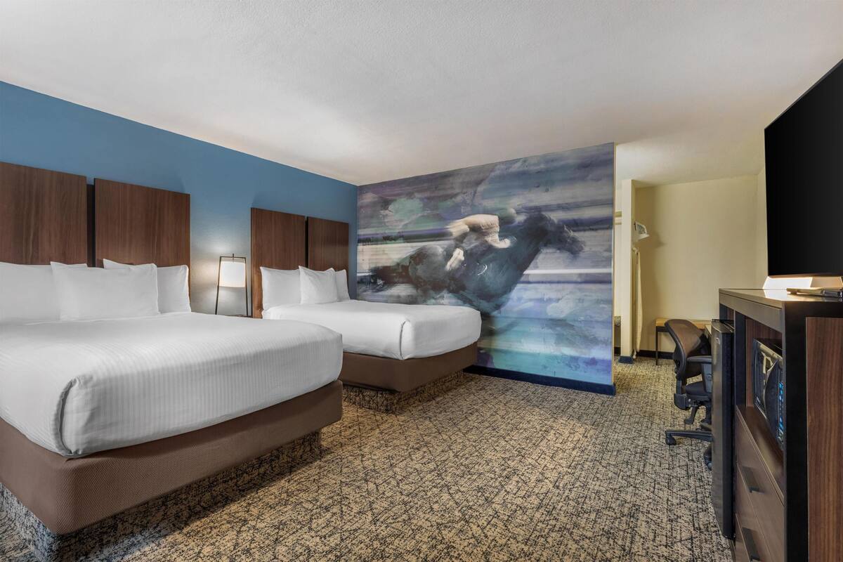 A hotel room with two beds, a desk, a chair, a TV, and a large abstract painting on the wall.