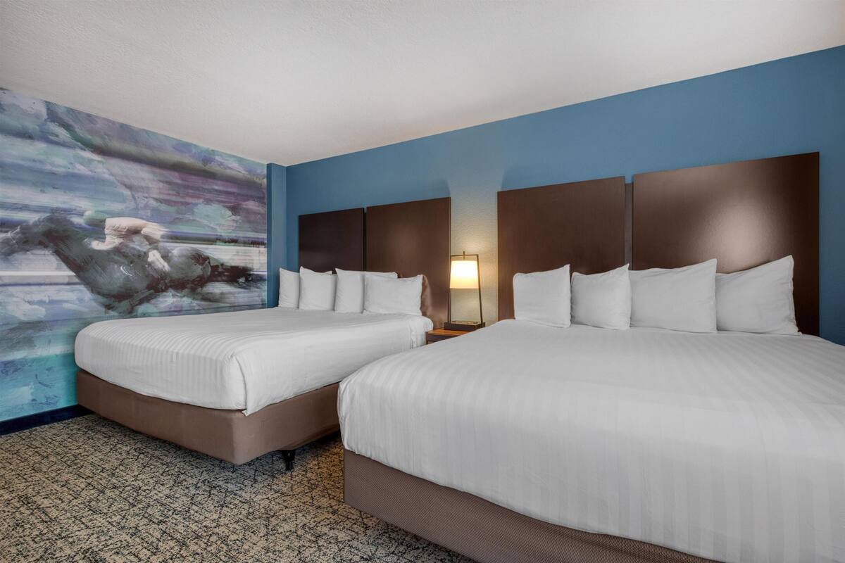A hotel room with two beds, a large abstract painting on the wall, and a patterned carpet.