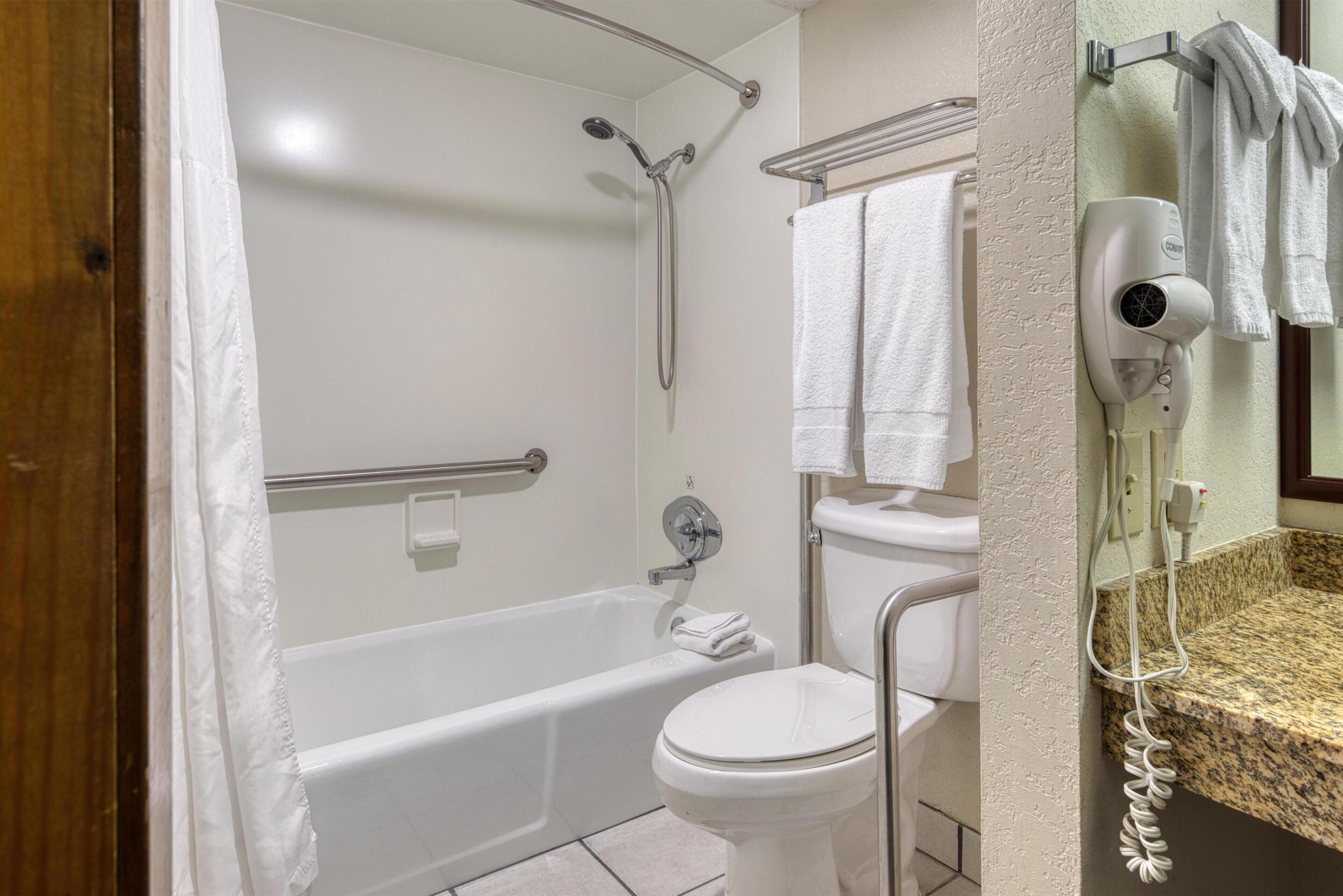 Un baño con bañera, inodoro y un secador de pelo en la pared.