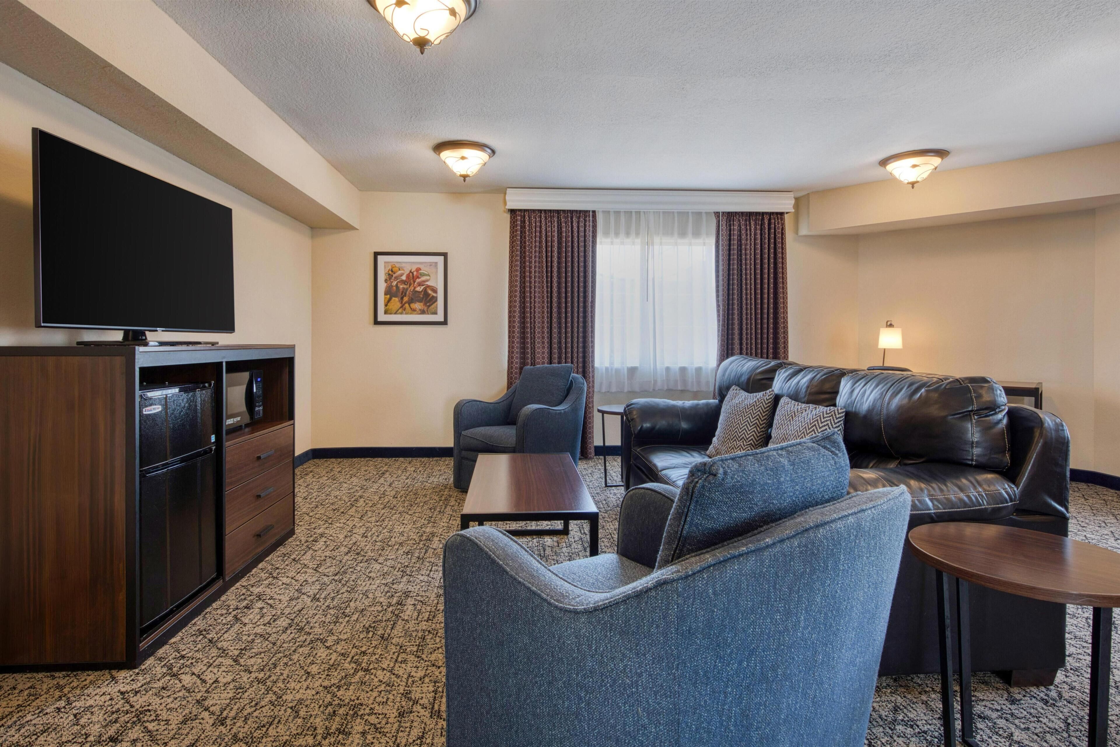 A hotel room with a flat-screen TV, a sofa, a chair, a small table, and a cabinet.