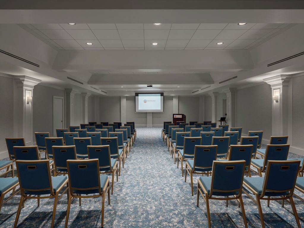 Un salón de conferencias con filas de sillas azules y piso alfombrado.