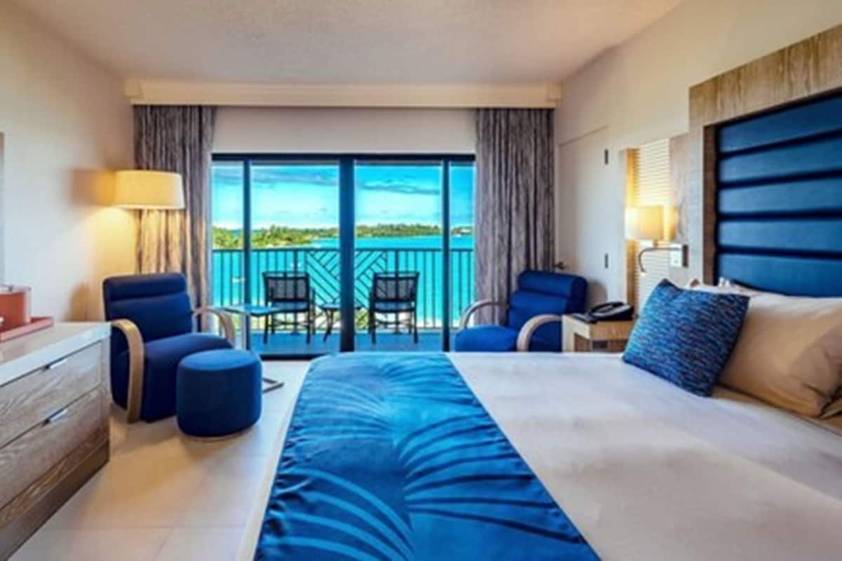 A hotel room with a large bed, a TV, a desk, and a balcony with chairs.