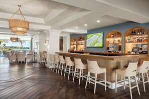 A bar area with a wooden counter, bar stools, and a large screen displaying a map.