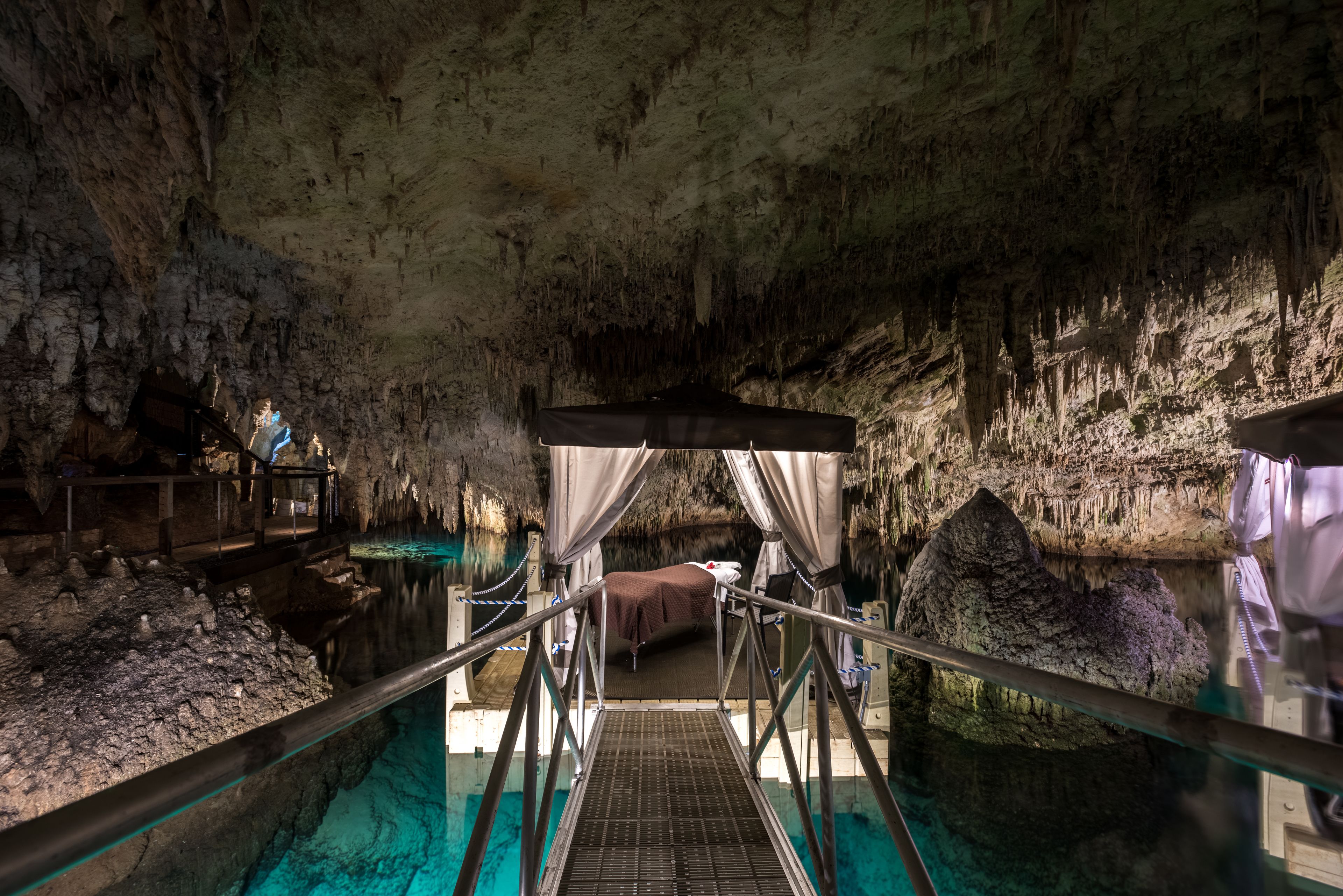 A cave with a glass walkway leading to a bed under a canopy.